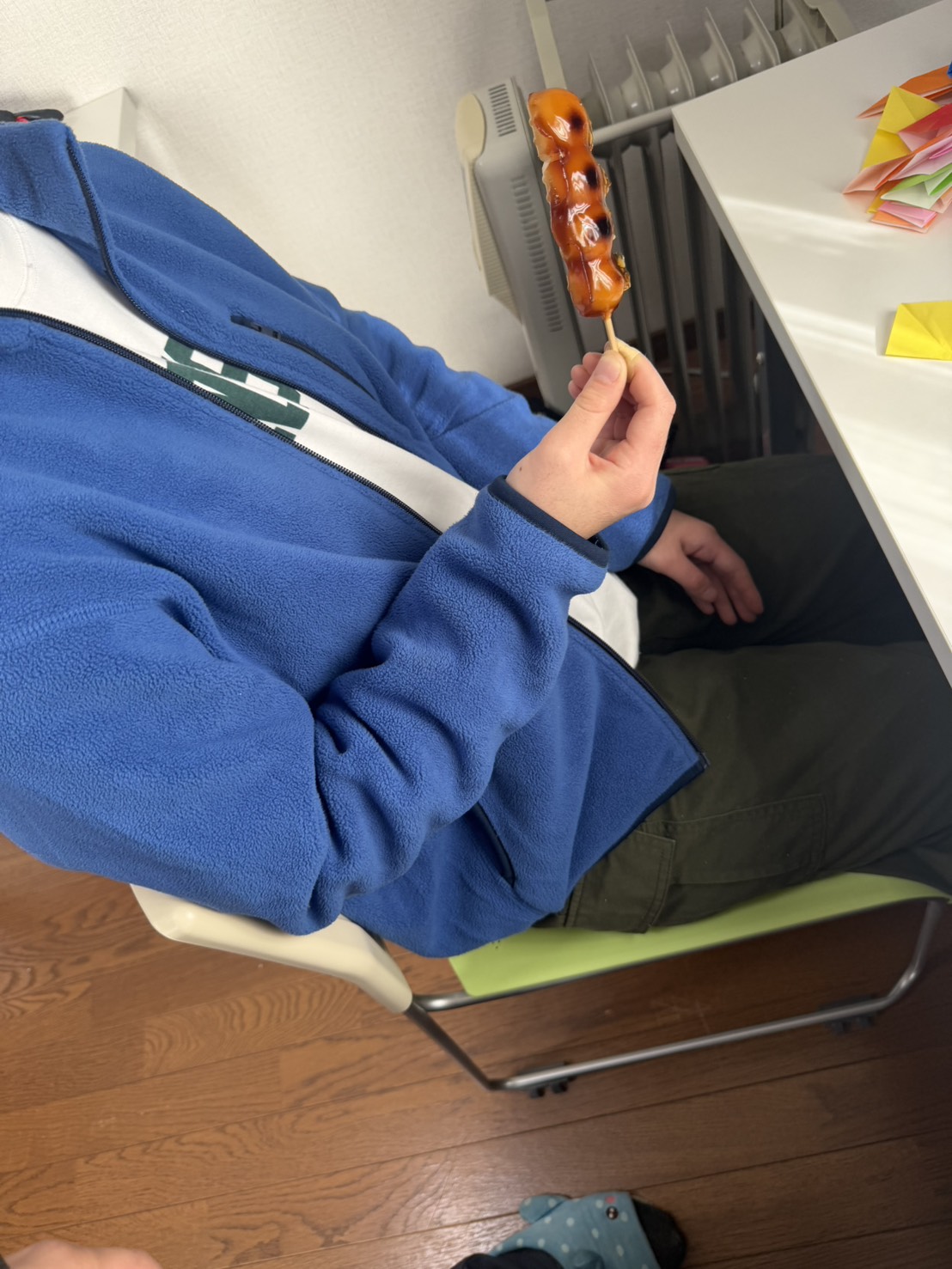 ブルーの上着を着た利用者がみたらし団子を手に持ち、机の横でくつろいでいる様子